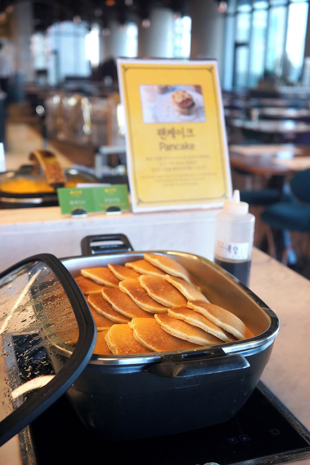 Et buffetområde med et skilt til pandekager og en overdækket serveringsskål med pandekager.