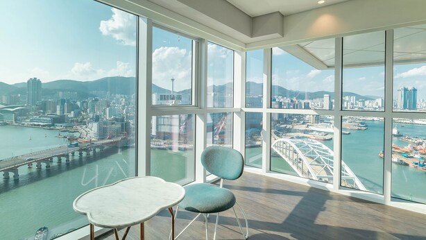 Um quarto espaçoso com grandes janelas que oferecem vista para a cidade, incluindo uma ponte e a orla marítima.
