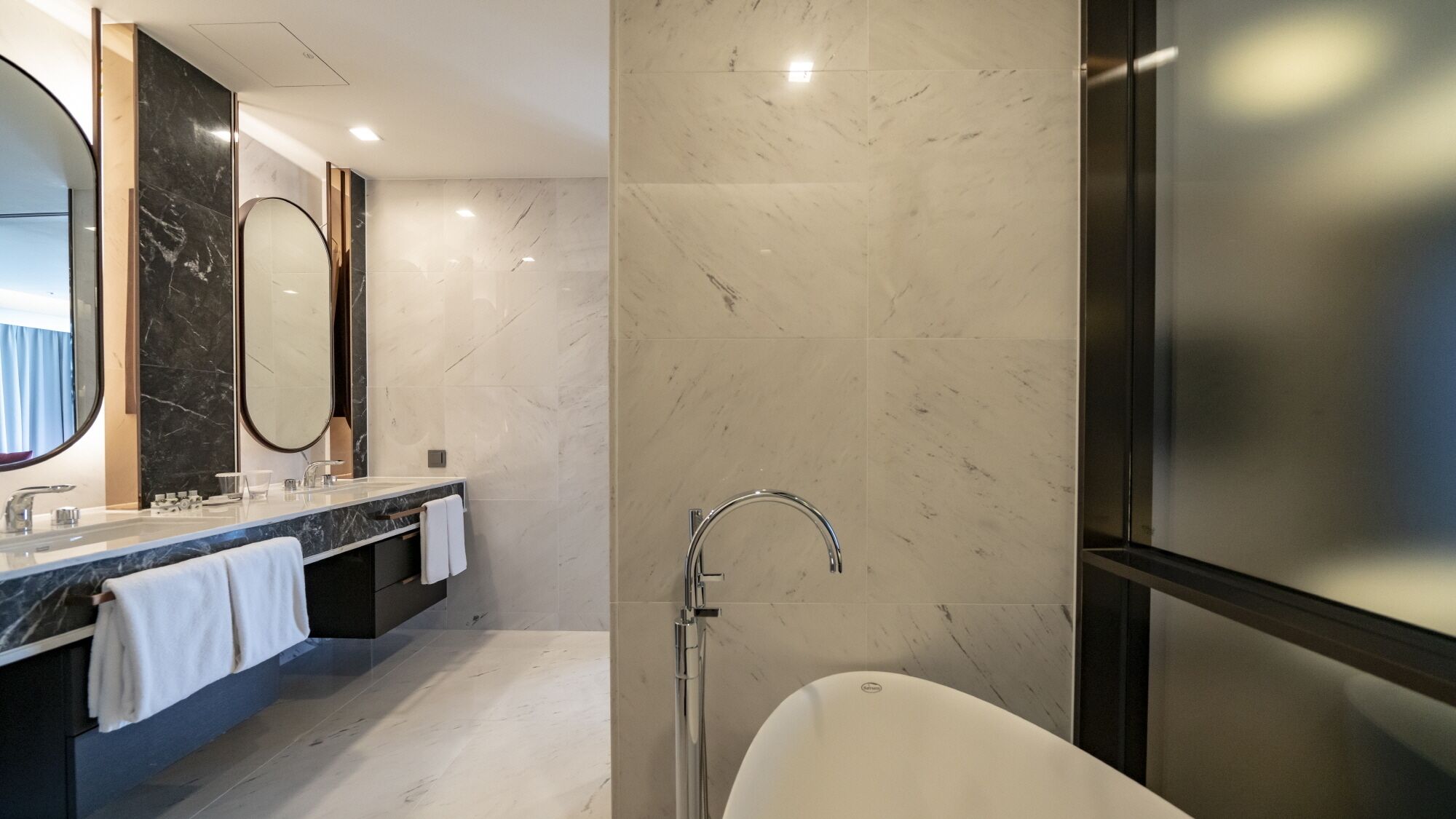 Een moderne badkamer met een marmeren wastafel, een grote spiegel en een vrijstaand bad.