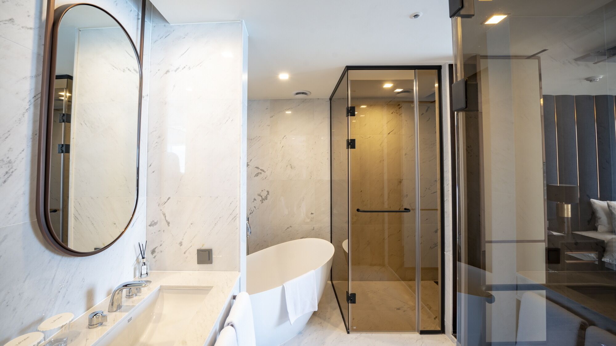 Un baño moderno con una bañera ovalada grande, una ducha con mampara de vidrio y un espejo amplio.