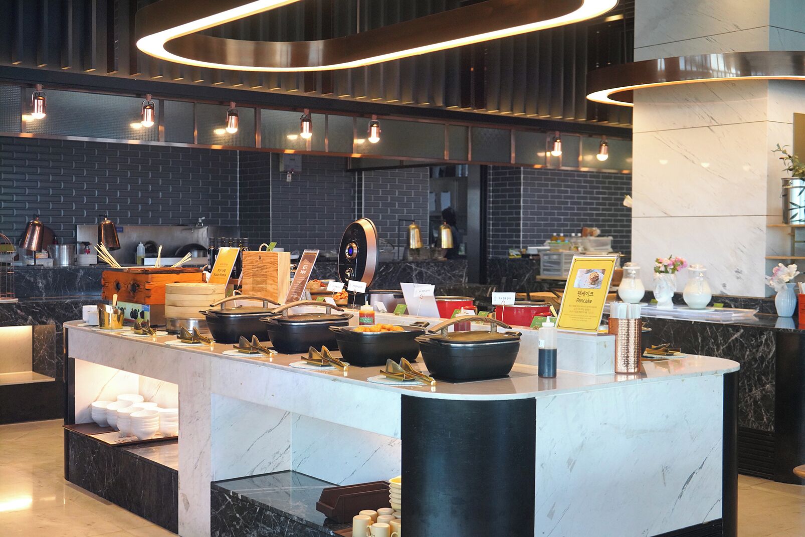 A buffet setup with various food containers and utensils, a marble counter, and overhead lighting.