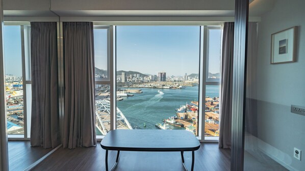 A spacious room with a large window offering a view of a coastal cityscape, including a bridge and port.