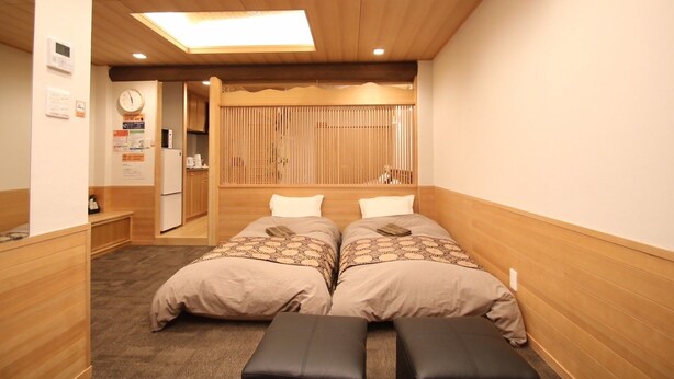 A hotel room with a wooden ceiling, two beds with patterned bedding, a bench, a clock, and a small kitchenette. - Kyoto Guest House Gion (Kyoto)