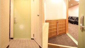 A hotel hallway with a green door, a wooden bench, and a seating area with black chairs. - Kyoto Guest House Gion (Kyoto)
