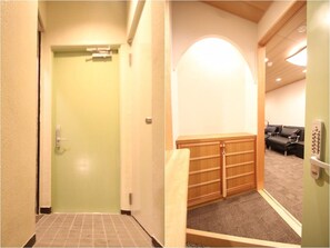 Enter a cozy space with a green door leading to a hallway, featuring a seating area with a bench and a wooden cabinet with drawers.