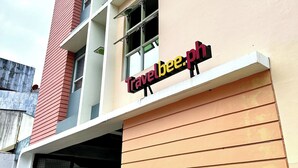 A building with a Travelbee.ph sign, a garage entrance, and potted plants. - Travelbee Fuente Inn (Cebu City)