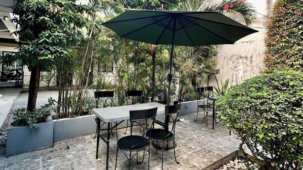 An outdoor patio with a table and chairs under a green umbrella, surrounded by lush greenery and stone flooring. - Travelbee Fuente Inn (Cebu City)