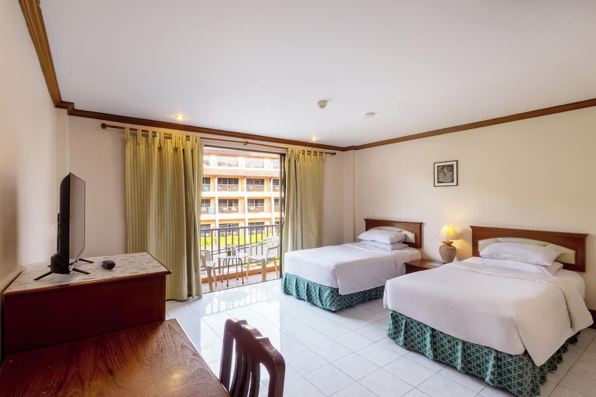 Habitación de hotel con dos camas, televisión, escritorio y balcón con vistas a un edificio.
