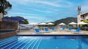Una piscina amb rajoles blaves, envoltada de gandules i ombrel·les, amb una vista de muntanya al fons.
