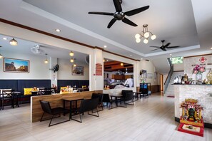 A restaurant with wooden tables and black chairs, a counter with a cash register, and a decorative altar on the right. - Kata Sun Beach Hotel (Karon)