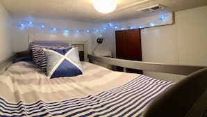 A bedroom with a bed, a nightstand, a lamp, and string lights. - Cozy cottage on the lake (Liberty Hill)