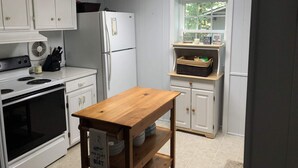 A compact kitchen with white cabinets, a refrigerator, a stove, and a wooden table. - Cozy cottage on the lake (Liberty Hill)