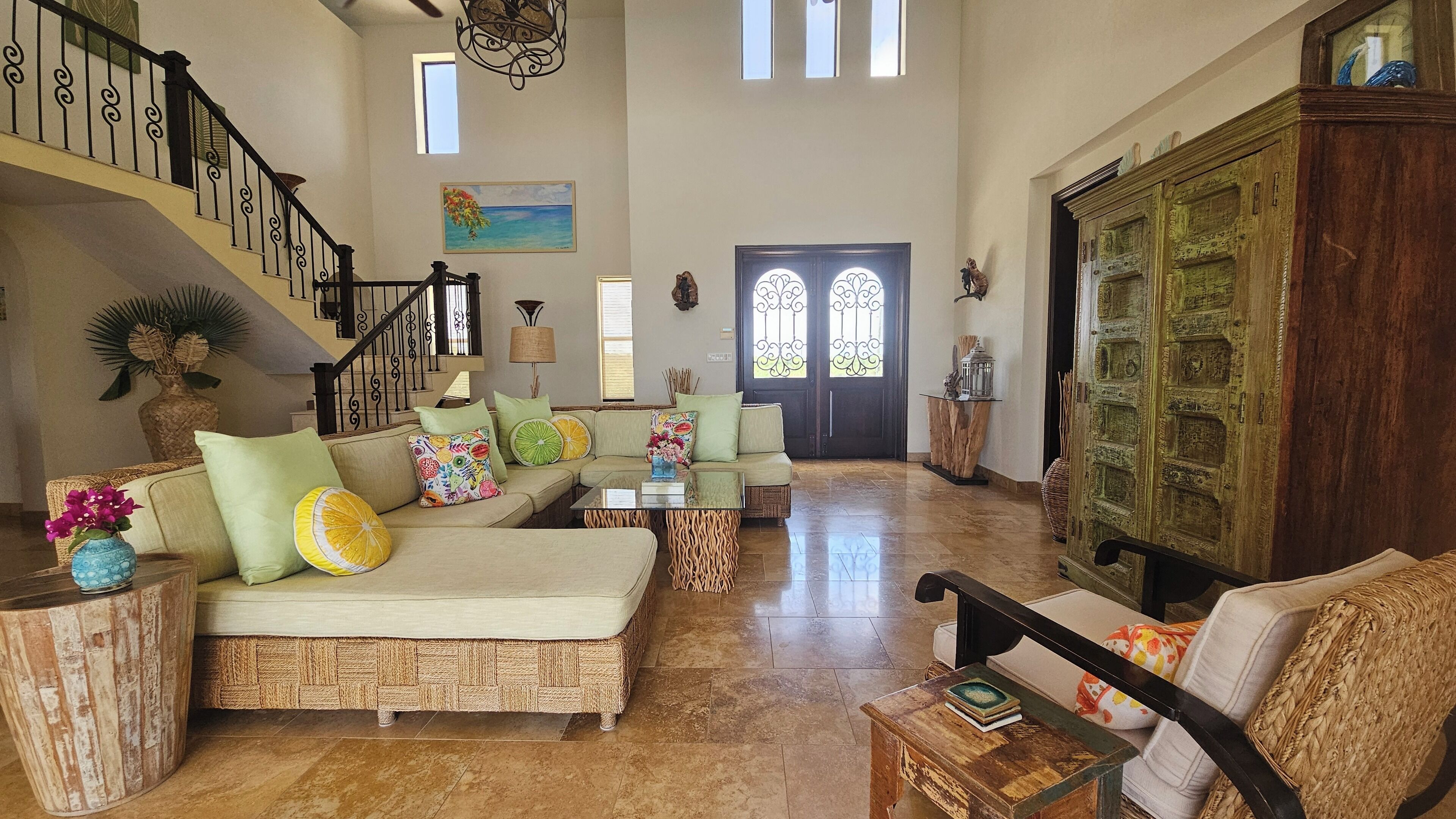 A spacious living room with a high ceiling, a staircase, and a large wooden cabinet.
