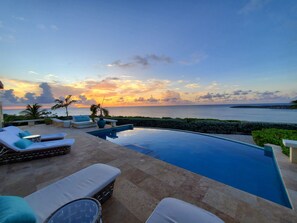 A poolside area with lounge chairs and a view of the sea at sunset. - Panoramic view of Crocus Bay; spacious; private; heated pool (Katouche Bay)