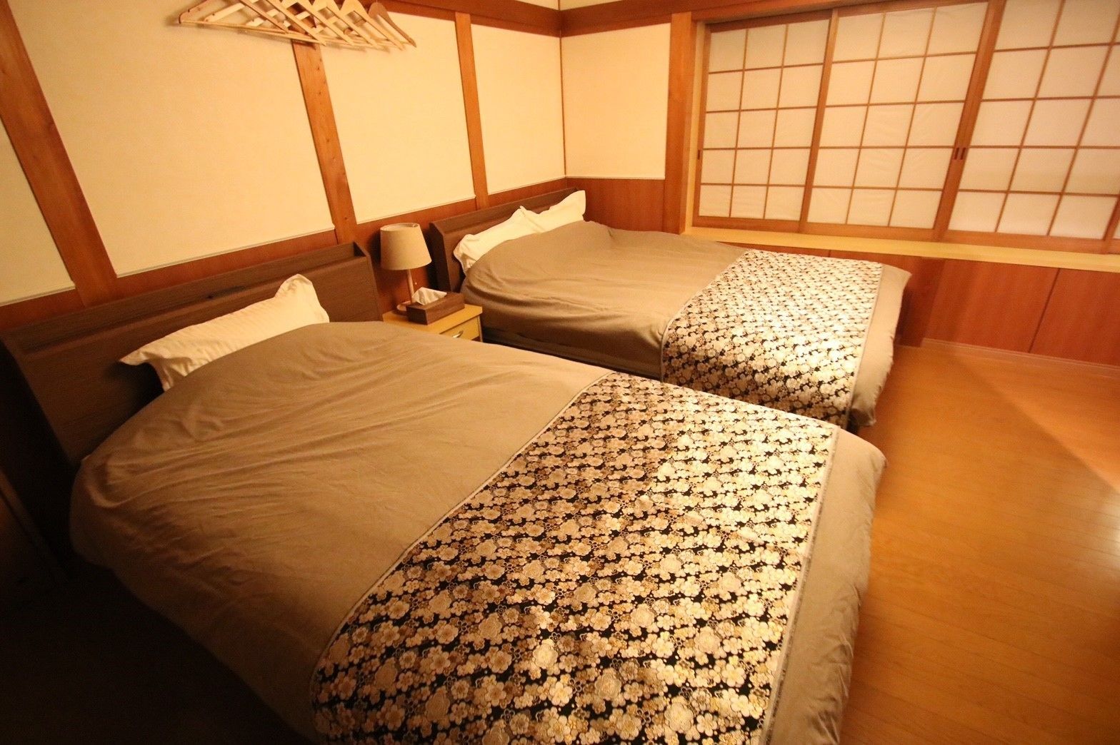 A room with two beds, wooden headboards, a bedside table with a lamp, and a shoji screen.