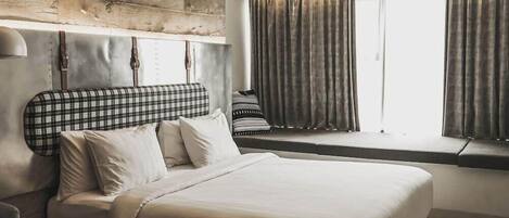 A modern hotel room with a large bed, a headboard with a plaid pattern, a window with curtains, and a wooden accent wall.