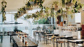 A spacious restaurant with long wooden tables and chairs, hanging plants, and a view of the outdoors. - PULANG ke UTTARA (Depok)