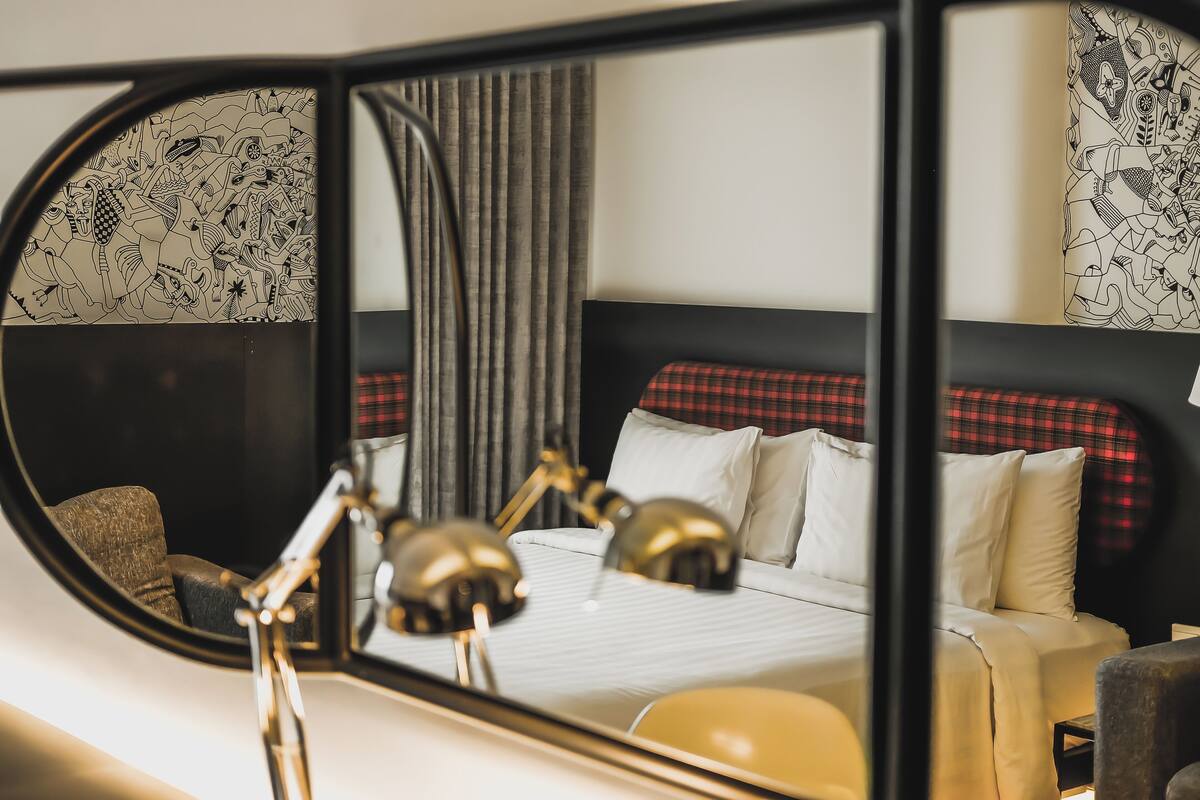 A hotel room with a bed, a mirror, and a lamp.