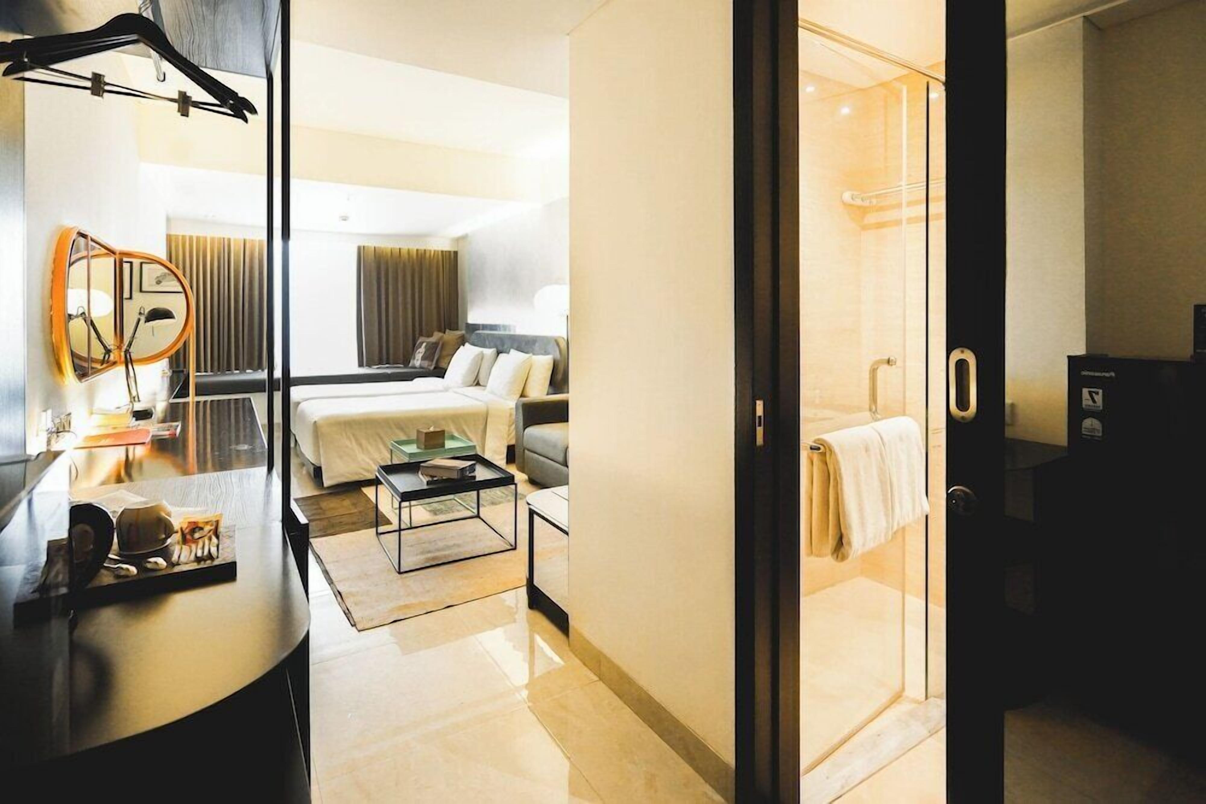Une chambre d’hôtel comprenant un lit, un canapé, une table basse, un miroir et une douche séparée par des parois en verre.