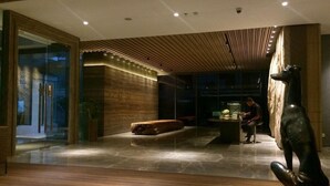 A modern lobby with a wooden ceiling, a glass wall, and a large sculpture. - PULANG ke UTTARA (Depok)