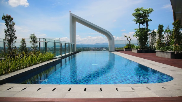 A modern infinity pool with a glass railing, surrounded by greenery and a clear view of the cityscape. - PULANG ke UTTARA (Depok)