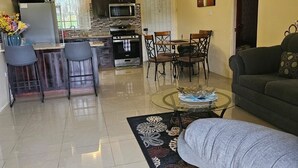 A spacious living area with a dining table, chairs, a sofa, and a kitchen in the background. - Crimson Heights is a three bedroom house, in a Secured Gated Community (St Ann’s Bay)