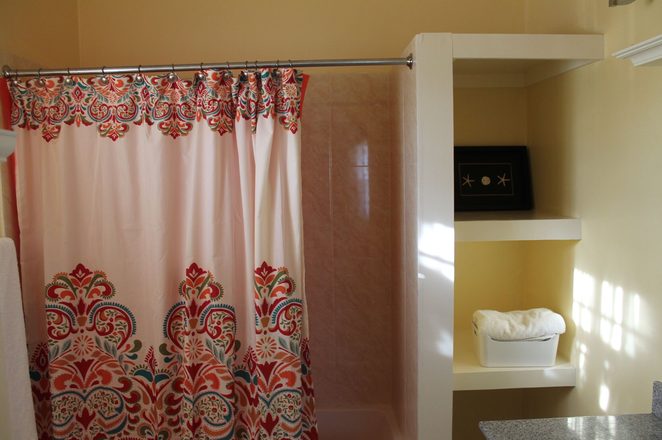 A bathroom with a shower curtain featuring a paisley pattern, a white shelf with a white towel, and a framed picture on the wall.
