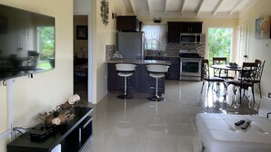 A modern kitchen with dark cabinets, a stainless steel refrigerator, and a microwave. There is a dining area with a white table and chairs. - Crimson Heights is a three bedroom house, in a Secured Gated Community (St Ann’s Bay)