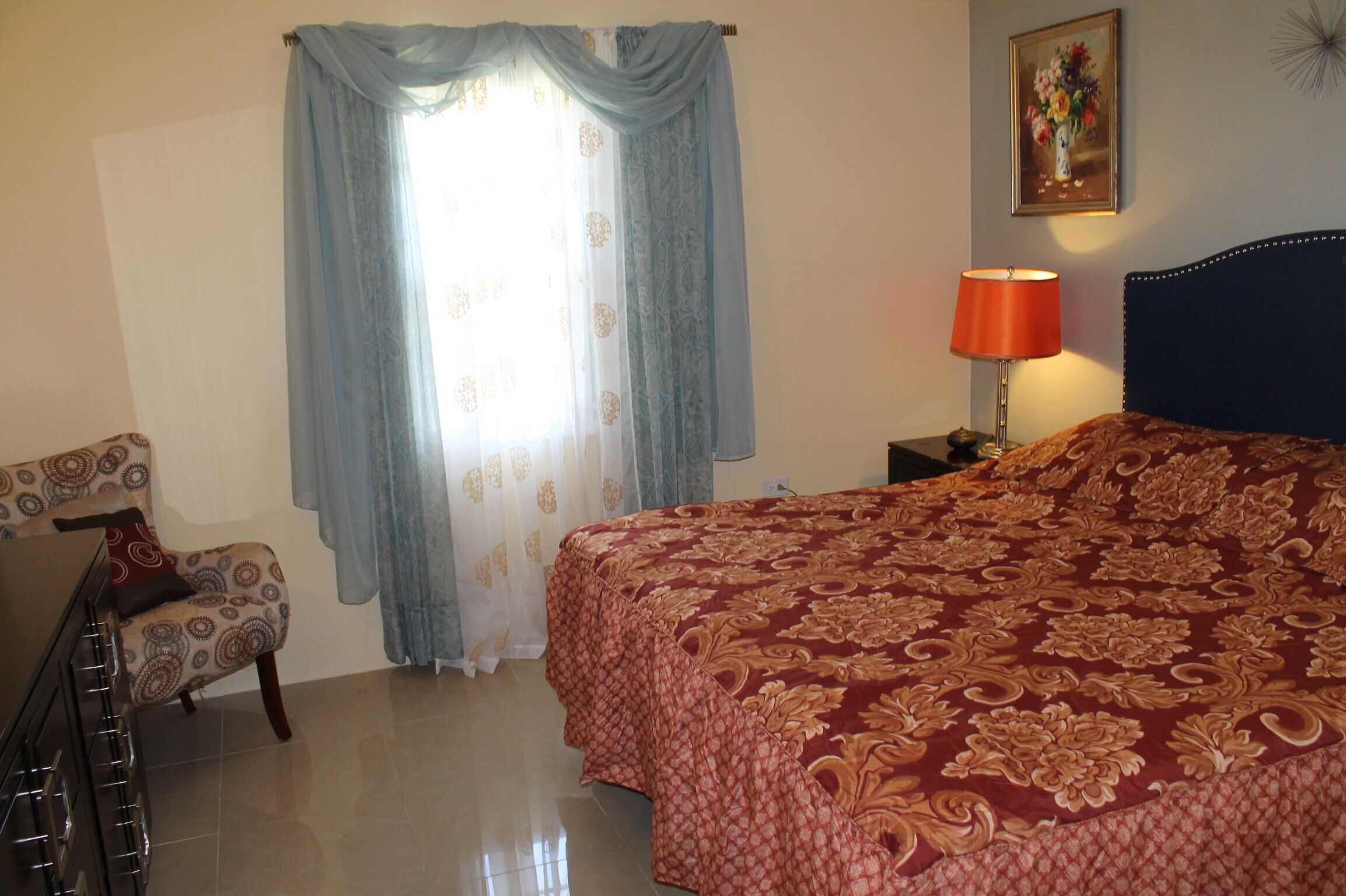 A bedroom with a bed, a chair, a lamp, and a painting on the wall.