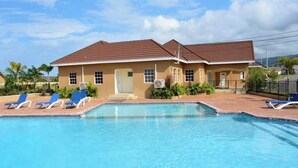 A two-story building with a swimming pool and lounge chairs. - Crimson Heights is a three bedroom house, in a Secured Gated Community (St Ann’s Bay)