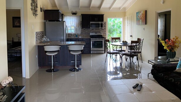 A modern kitchen with a central island, bar stools, and a dining area with a table and chairs. - Crimson Heights is a three bedroom house, in a Secured Gated Community (St Ann’s Bay)