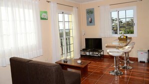 Una sala de estar con sofá, mesa de centro, televisor y zona de comedor con mesa y dos taburetes de bar.