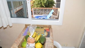 Una encimera de cocina con una cesta de frutas y verduras frescas, pan empaquetado y una lista de compras.