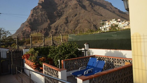 Un balcón con vista a una montaña, un portón y un edificio de paredes blancas y techo verde.