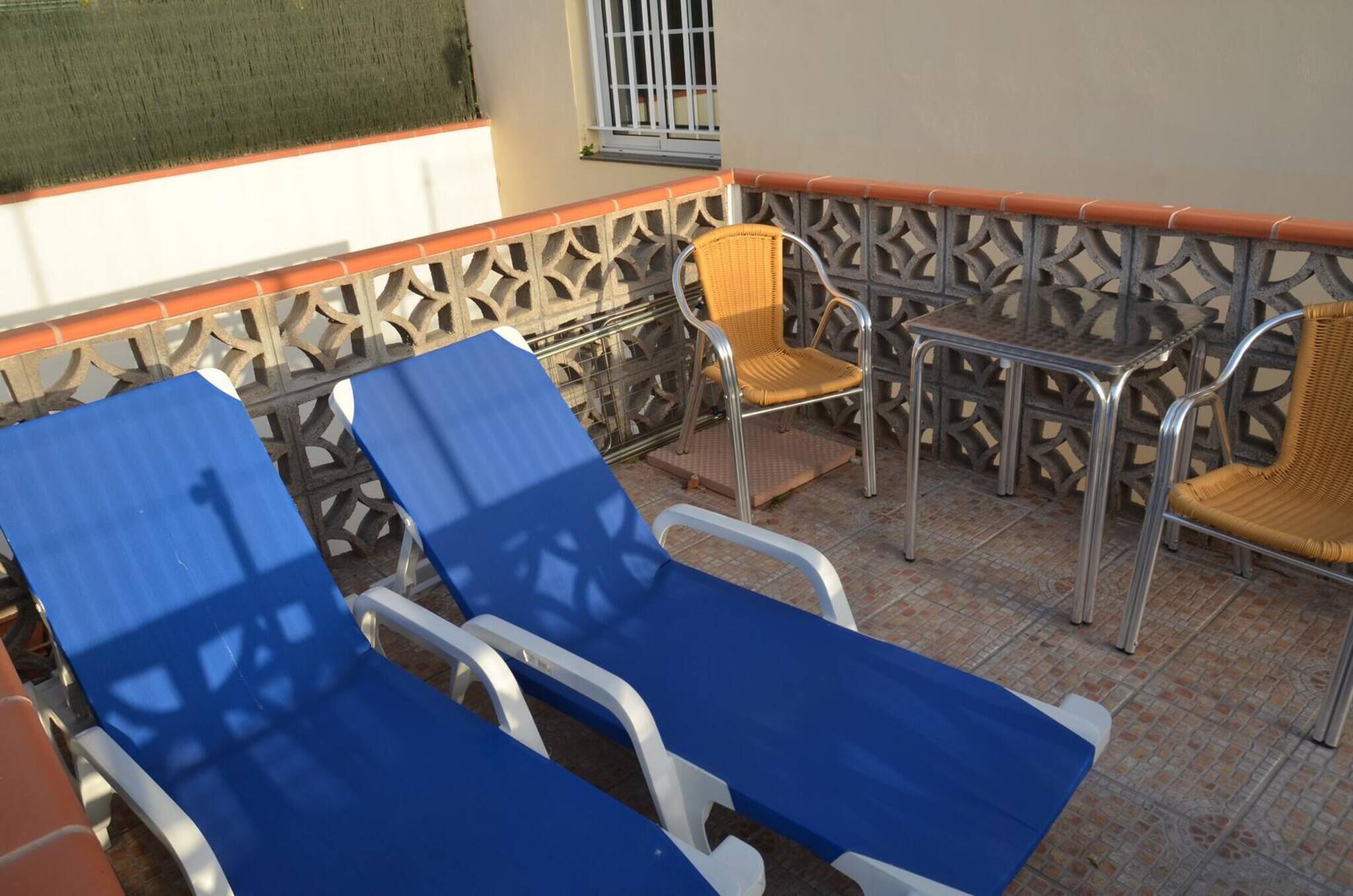 A balcony with blue lounge chairs, a wicker chair, and a metal table.