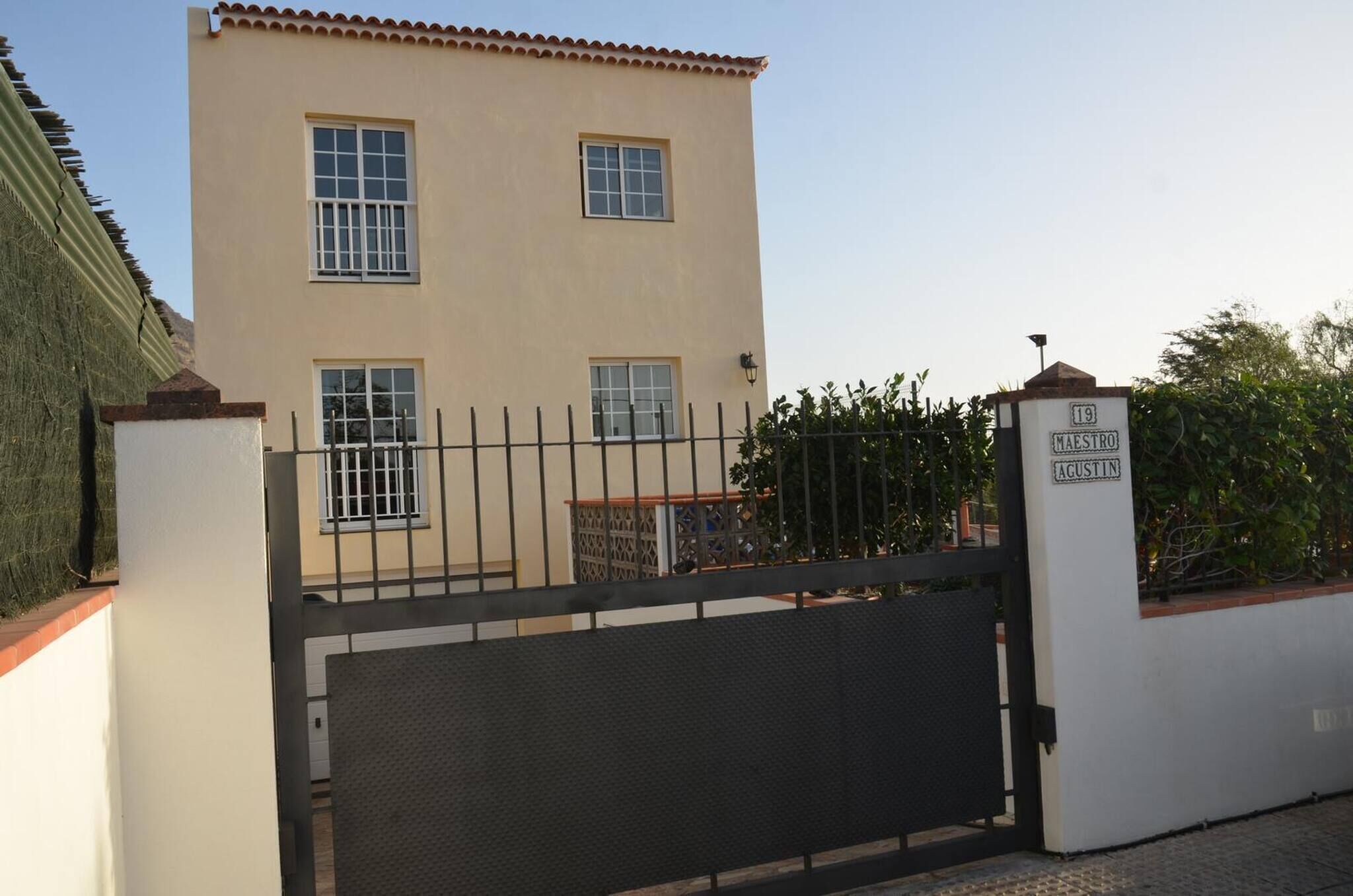 A two-story building with a beige facade, a gated entrance, and a sign indicating 'MAESTRO AGUSTIN'.