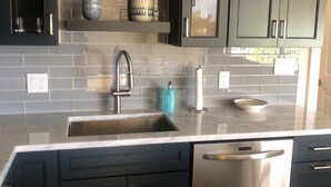 A modern kitchen with dark cabinets, a stainless steel dishwasher, and a tiled backsplash. - 5th Fl condo, steps to JW Marriott & Beach, Sunset Views, walk to restaurants (Marco Island)
