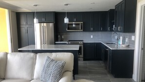 A modern kitchen with dark cabinets, stainless steel appliances, and a grey tiled backsplash. - 5th Fl condo, steps to JW Marriott & Beach, Sunset Views, walk to restaurants (Marco Island)
