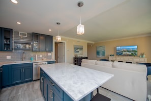 A modern kitchen with blue cabinets, a marble island, and pendant lighting.