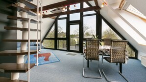 A spacious attic room with a sloped ceiling, large windows, a wooden staircase, and wicker chairs. - RügenHeart 3 Dachträume - RügenHeart 3 Dachträume (Parchtitz)
