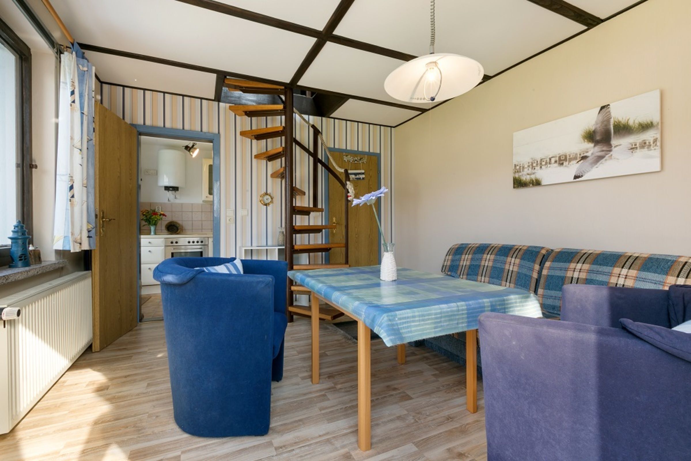 Eine kompakte Küche mit einer Holztreppe, einem Essbereich mit Tisch und Stühlen sowie einer Couch.