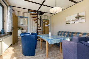 A compact kitchen with a wooden staircase, a dining area with a table and chairs, and a sofa.