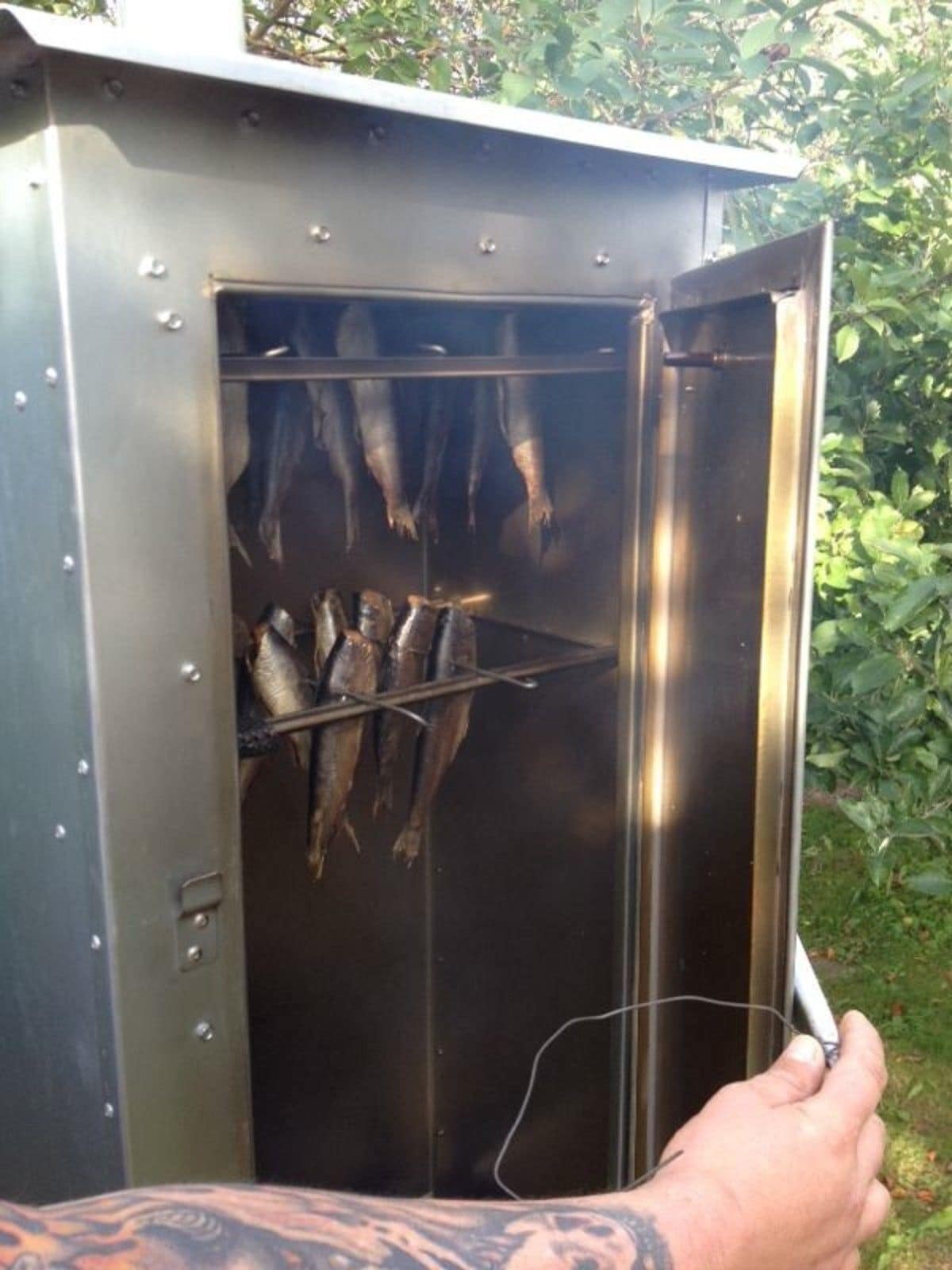Ein Outdoor-Grill aus Metall mit Fisch, der in Aufhängenetzen darin hängt.