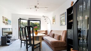 A modern living room with a sofa, a dining table, and a TV. There is a cabinet with glass doors and a chandelier. - RügenHeart 2 Piratenhaus - RügenHeart 2 Piratenhaus (Parchtitz)
