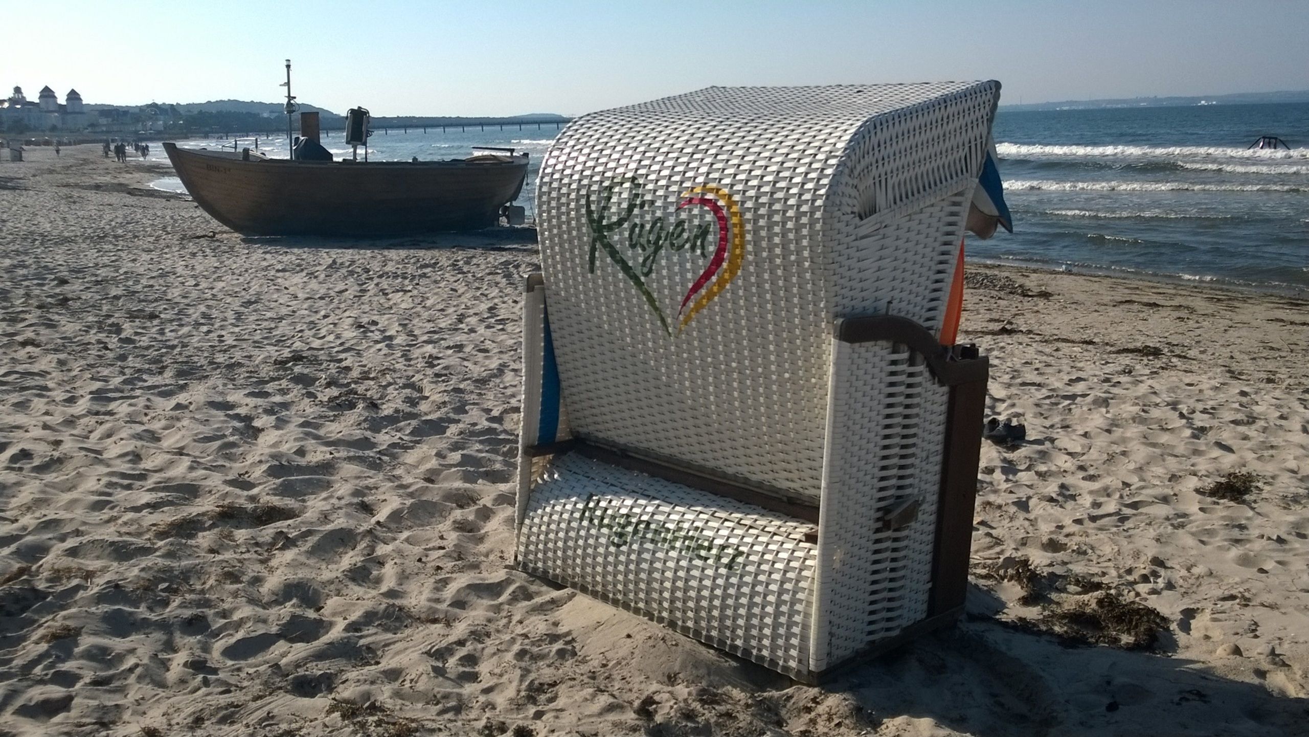 En strandstol med et logo, en båd i baggrunden og en sandstrand.