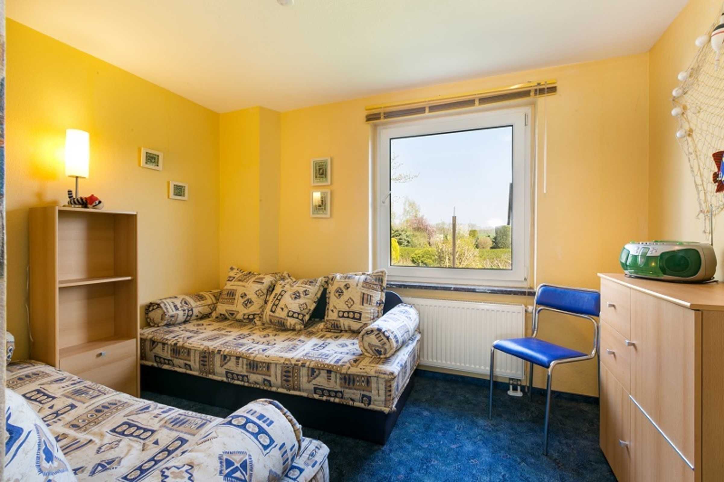 Une pièce comprenant un canapé-lit, un fauteuil, un radiateur, une fenêtre donnant sur un paysage agréable et une étagère avec une lampe.