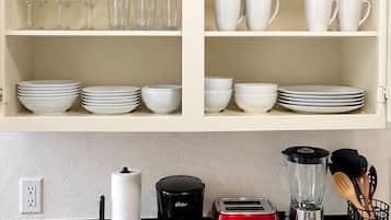 A kitchen with a white cabinet containing various dishes and glasses, a black countertop with a coffee maker, toaster, and blender, and a black backsplash.