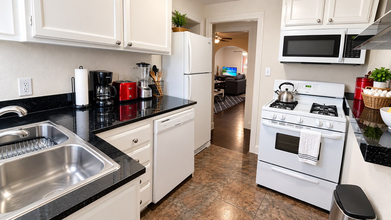A kitchen with a stainless steel sink, white cabinets, a stove, and a microwave.