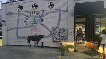 A building with a mural titled 'The Pit Room' featuring a cow and a woman. There are potted plants in front and a person entering the building.