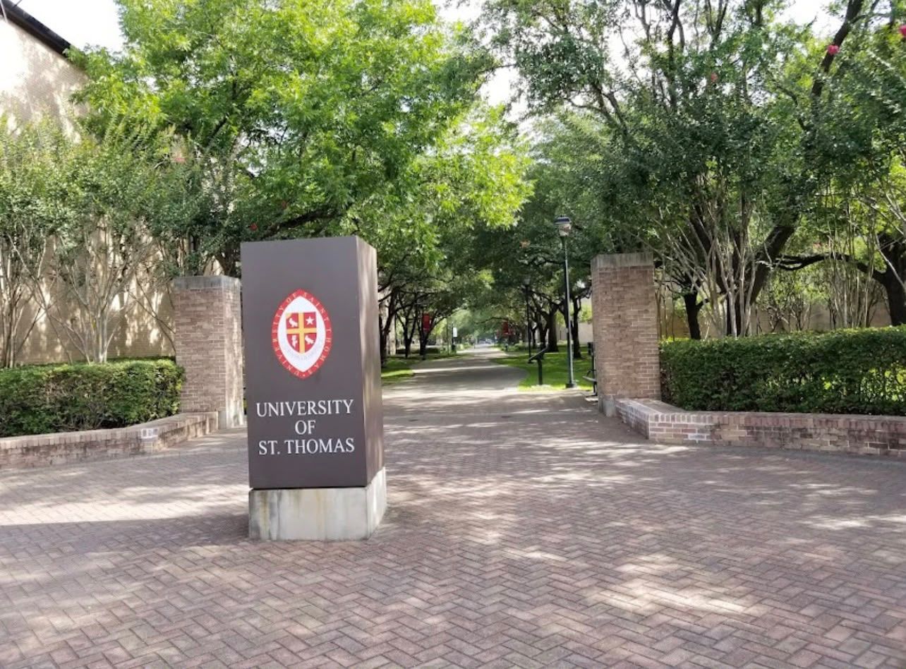 A sign for the University of St. Thomas with a brick pathway leading to it.